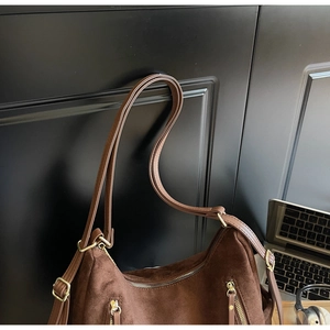 Detail of dark brown suede shoulder bag with gold zippers and adjustable strap
