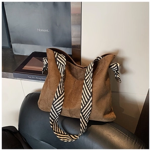 Close-up of a large brown matte suede tote bag with striped straps on a leather chair
