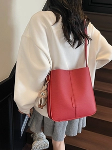 Sac seau en cuir grainé rouge avec pendentif pompon marron porté en bandoulière