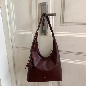 Détail du sac hobo en cuir bordeaux foncé avec logo de marque suspendu à une porte