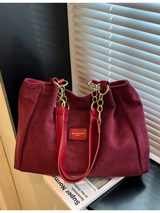 Large burgundy suede tote bag with golden chain and branding in minimalist setting