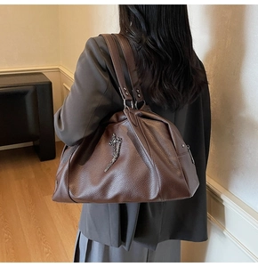 Detail of dark brown tote bag featuring pebbled leather and metal cross chain pendant
