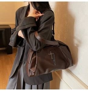 Detail of dark brown pebble leather handbag featuring a vintage silver cross and tassel