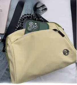 Close-up of beige crossbody bag showing spacious front zipper pocket and metal M logo