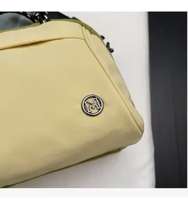 Detail of light yellow canvas bag with green trim and metallic M logo embellishment