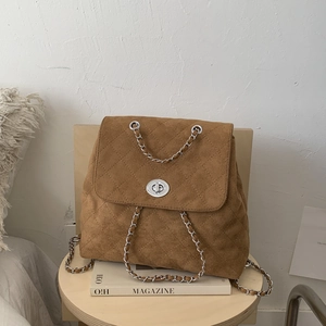 Détail d'un sac à dos en daim marron avec matelassage et chaîne sur un tabouret en bois