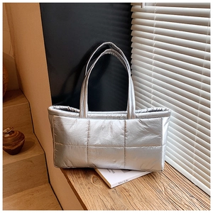 Detailed view of silver puffer tote bag featuring quilted texture in a sunlit indoor setting