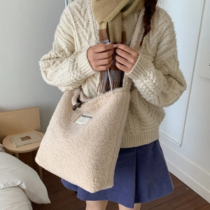 Detail shot of beige faux shearling tote bag with a SEEYOU woven label on plush fabric