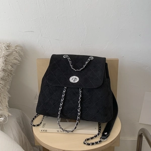 Détail du sac à dos matelassé en daim noir avec bandoulière chaîne sur tabouret