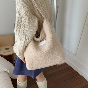 Model wearing a large beige fuzzy sherpa tote bag with SEEYOU label in cozy room