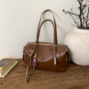 Detail of dark brown glossy leather Boston bag with silver hardware and colorful charms