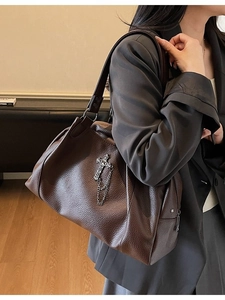 Dark brown leather tote bag with silver cross and metal chain details worn by a model