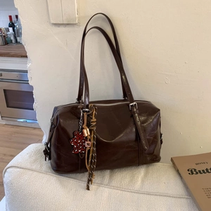 Detail of dark brown glossy leather underarm bag with red leopard print bear pendant