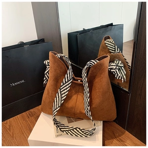 Detail of a brown suede tote bag featuring a black and white twill woven shoulder strap