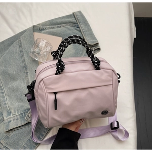 Detail of lavender nylon crossbody bag with woven rope handle on white bedding