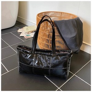 Detail view of large black glossy puffer tote bag with quilted texture and soft padded straps