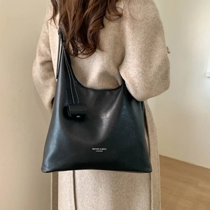 Dettaglio borsa a spalla in pelle nera con logo abbinata a un cappotto in lana beige