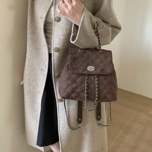 Détail du sac à dos en daim marron foncé surpiqué avec fermoir rotatif et bandoulière chaîne