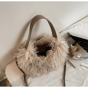 Detail of soft cream faux fur tote bag with brown leather straps on a bed setting
