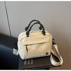 Minimalist beige nylon crossbody bag featuring a woven rope handle on a book background