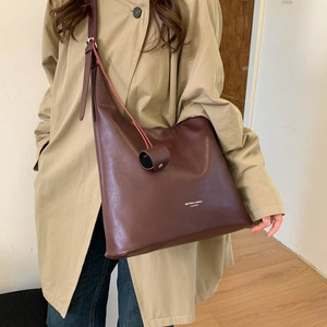 Dettaglio di una borsa tote grande in pelle marrone scuro con ciondolo indossata da modella