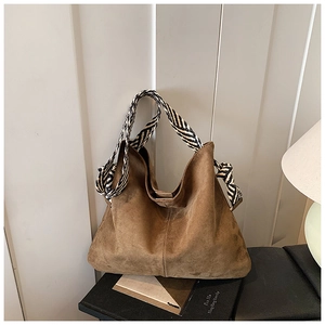 Detail of a brown suede hobo bag featuring a black and white woven rope shoulder strap