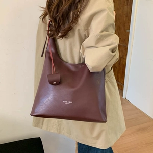 Dettaglio della borsa tote in pelle marrone scuro con logo e pochette piccola appesa