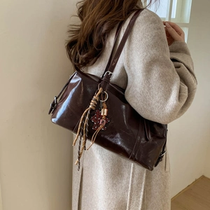 Detail of dark brown polished leather shoulder bag with decorative woven pendant