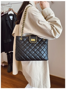 Gros plan d'un sac à bandoulière noir matelassé avec chaîne dorée porté sur un trench beige
