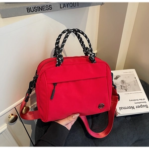 Detail of red nylon crossbody bag with braided handle and metallic logo emblem