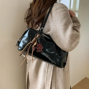 Detail of black glossy faux leather shoulder bag featuring a red leopard print bear charm