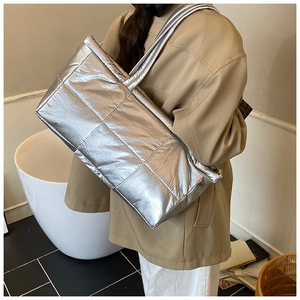 Detailed view of silver metallic quilted tote bag worn with a classic khaki trench coat