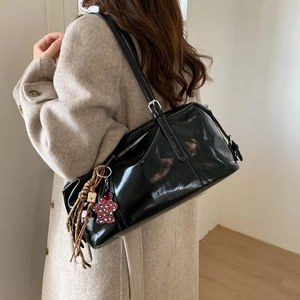 Side view of black glossy patent leather shoulder bag with leopard charm on a model