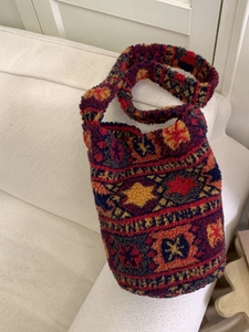 Fuzzy plush bucket tote bag with colorful geometric patterns on a beige sofa