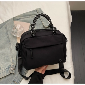 Detail of black crossbody bag with woven handle and metallic M logo on bed