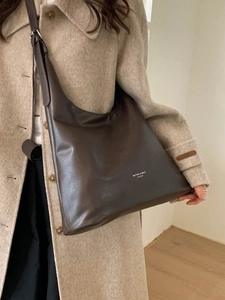 Borsa hobo marrone scuro in pelle opaca con logo bianco indossata su cappotto beige