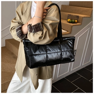 Close-up of a large black quilted tote bag with a glossy finish on a fashion model