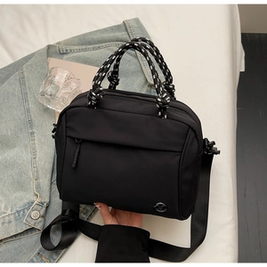 Detailed shot of a black nylon crossbody bag with braided handles on a soft fabric background