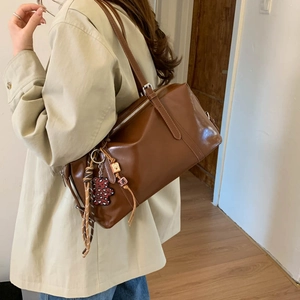 Detail of a brown leather shoulder bag with colorful bead pendants and a teddy bear charm