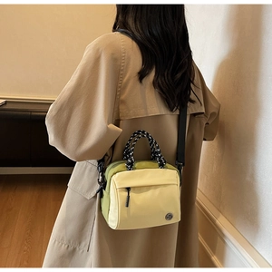 Crossbody bag with green side panels and woven handle shown on trench coat model