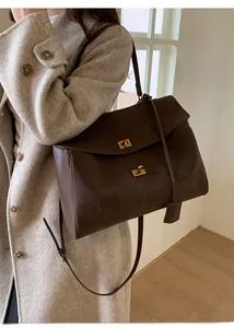 Detail of dark brown matte leather tote bag showing metallic gold clasps and shoulder strap
