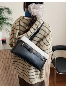 Detail view of black faux leather shoulder bag with white plush trim and gold buckle worn by model
