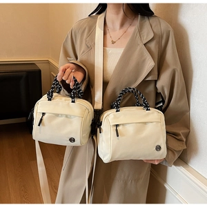 Close-up of cream crossbody bag with woven knot handle and circular metal M logo detail