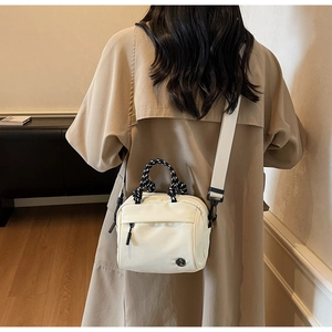 Detail of a creamy white crossbody bag with woven handles and wide nylon shoulder strap