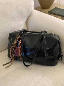 Glossy black leather Boston bag with trendy charms on a white textured sofa
