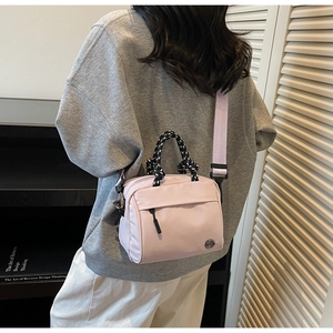 Detail of light pink nylon crossbody bag with black and white woven handle and logo