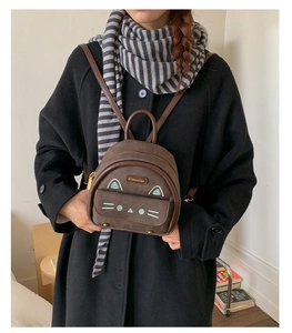 Detail of a brown mini backpack with cute cat embroidery and brand label on suede material