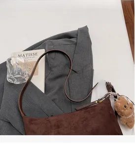 Details der braunen Wildleder-Beuteltasche mit kleinem Bärenanhänger und Schulterriemen