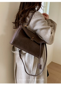 Macro detail of dark brown suede shoulder bag with gold hardware on beige coat