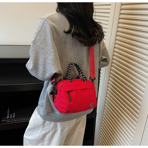 Detail of red nylon crossbody bag with woven handle and metallic M logo on a model